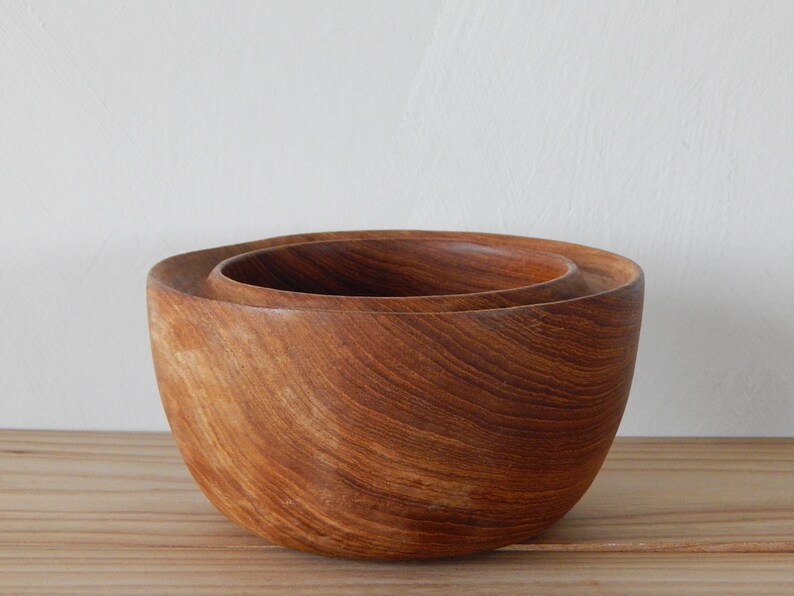 Puede incluir: Dos cuencos de madera, uno anidado dentro del otro. Los cuencos est&aacute;n hechos de madera marr&oacute;n oscura con un patr&oacute;n de veta natural.