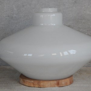 May include: White glass lampshade with a wide, rounded base and a narrow neck. The lampshade is sitting on a wooden base.