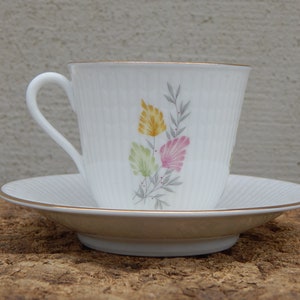 May include: A white teacup and saucer with a gold rim and a floral design. The flowers are pink, yellow, and green.