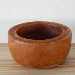 Puede incluir: Un cuenco de madera con un acabado marr&oacute;n natural. El cuenco tiene una forma redondeada y una superficie lisa y pulida.