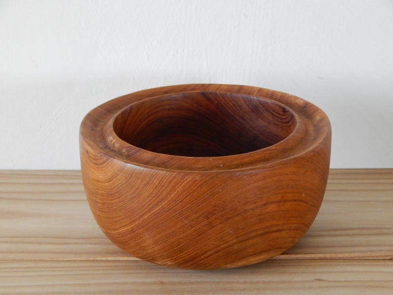 Puede incluir: Un cuenco de madera con un acabado marr&oacute;n natural. El cuenco tiene una forma redondeada y una superficie lisa y pulida.