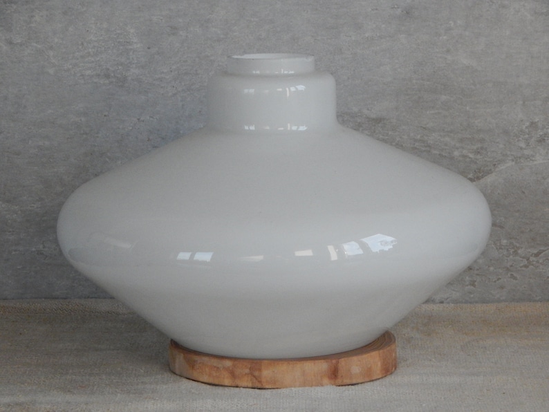 May include: White glass lampshade with a wide, rounded base and a narrow neck. The lampshade is sitting on a wooden base.