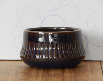 May include: A small, dark brown and blue ceramic bowl with a fluted design. The bowl is glazed and has a glossy finish.
