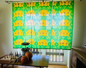 May include: Three rectangular window curtains featuring a repeating pattern of bright yellow flowers and green leaves on a vibrant green background, suspended from a silver metal curtain rod with circular rings and clips at the top edge.