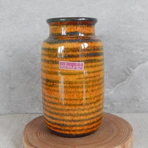 Puede incluir: Un jarrón de cerámica rayado en marrón y amarillo con un borde verde. El jarrón tiene una etiqueta que dice "scheurich".