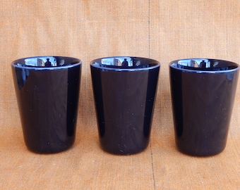 Puede incluir: Tres tazas de cerámica azul oscuro, cada una con un tono de azul ligeramente diferente, están alineadas en una fila sobre una superficie marrón.