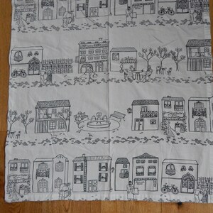 May include: Black and white fabric with a repeating pattern of a small town. The pattern includes houses, trees, people, bicycles, and a fountain.