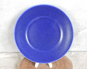 May include: A blue ceramic plate with a speckled glaze. The plate has a slightly raised rim and a centre well.
