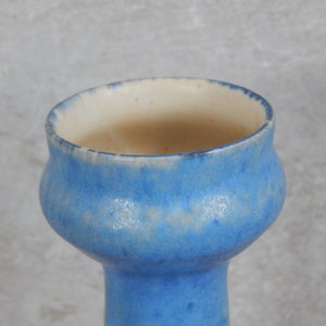 May include: A light blue ceramic vase with a white rim and a slightly flared opening. The vase has a speckled glaze.