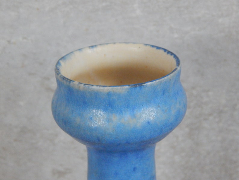 May include: A light blue ceramic vase with a white rim and a slightly flared opening. The vase has a speckled glaze.
