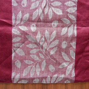 Pode incluir: Um corredor de mesa bordô com um padrão de folhas brancas. O corredor tem uma borda bordô.