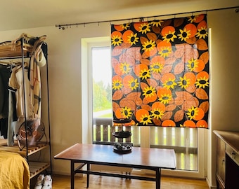 May include: A rectangular fabric panel featuring a repeating pattern of yellow sunflowers with black centers and orange circular shapes on a dark brown background, suspended from a metal curtain rod over a window in a room setting.