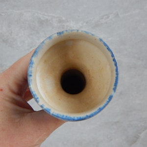 May include: A white ceramic vase with a blue rim. The vase has a wide opening and a narrow neck.