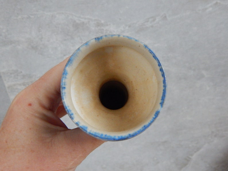 May include: A white ceramic vase with a blue rim. The vase has a wide opening and a narrow neck.