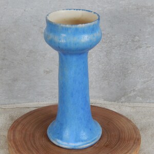 May include: A tall, light blue ceramic vase with a flared top and a rounded base. The vase has a mottled glaze and a white interior.