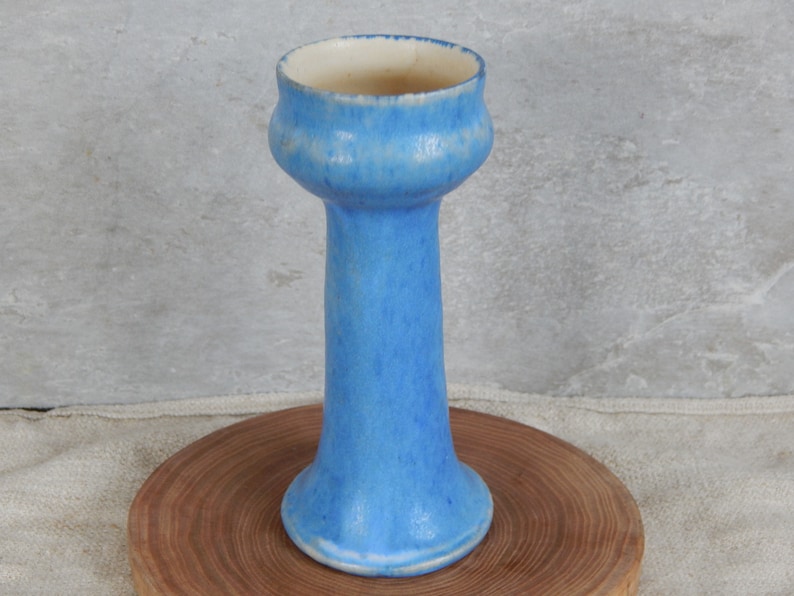 May include: A tall, light blue ceramic vase with a flared top and a rounded base. The vase has a mottled glaze and a white interior.