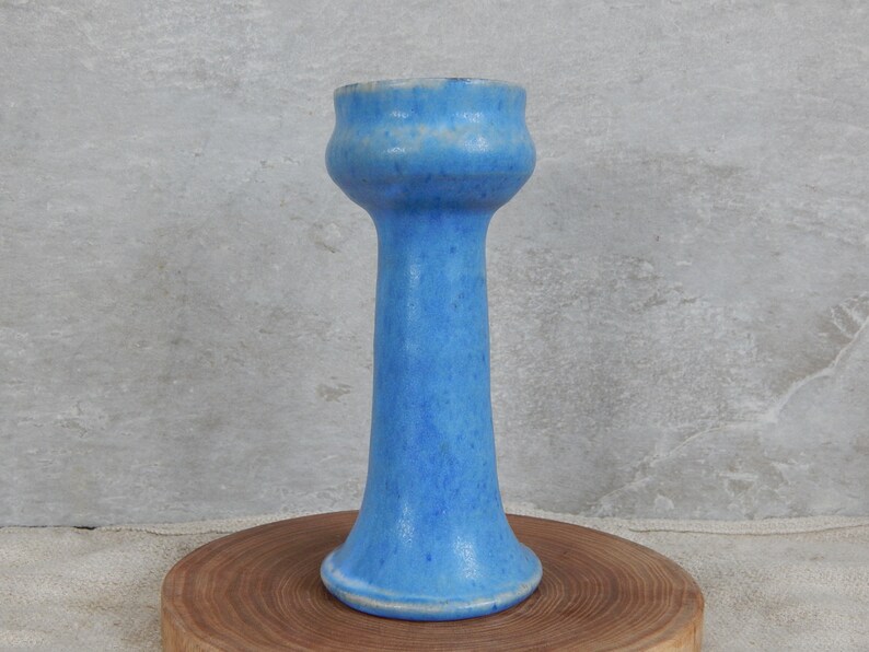 May include: A tall, light blue ceramic vase with a flared top and a wide base. The vase has a speckled glaze.
