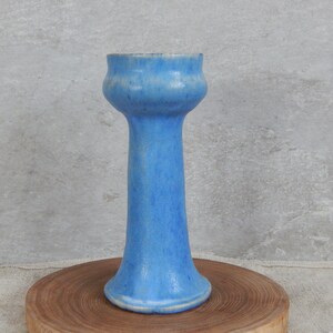 May include: A light blue ceramic vase with a flared top and a tall, slender body. The vase has a slightly textured surface.