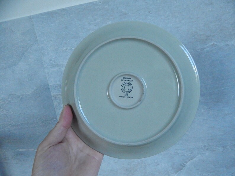 K&ouml;nnte beinhalten: Ein hellgr&uuml;ner Keramikteller mit einem blauen und wei&szlig;en Logo, auf dem unten "Rosendahl Denmark" und "Royal Copenhagen" steht.