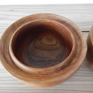 Puede incluir: Dos cuencos de madera con un acabado de madera natural. Los cuencos est&aacute;n anidados, con el cuenco m&aacute;s peque&ntilde;o dentro del m&aacute;s grande.