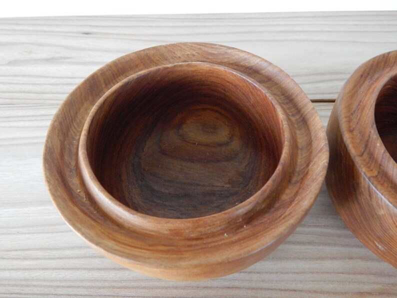 Puede incluir: Dos cuencos de madera con un acabado de madera natural. Los cuencos est&aacute;n anidados, con el cuenco m&aacute;s peque&ntilde;o dentro del m&aacute;s grande.