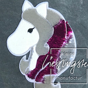 Puede incluir: Un parche de hierro de lentejuelas blancas y rosas con un caballo de dibujos animados con una melena y cola rosas. El parche tiene el texto "kleine lieblingsteile manufactur" en la parte inferior.