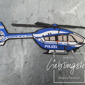 Könnte beinhalten: Blau-weiße gestickte Aufnäher eines Polizeihubschraubers mit dem Text "POLIZEI" und der Kennung "D-12XY3".