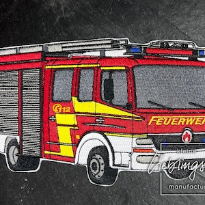 May include: Red and white fire truck with the word "FEUERWEHR" on the front. The truck has a ladder on top and a yellow stripe on the side. The truck is a patch.