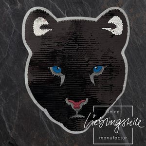 Op de afbeelding: Zwarte pailletten panterkop patch met blauwe ogen en een roze neus. De patch heeft een witte rand en de tekst "kleine lieblingsteile manufactur" is eronder gedrukt.