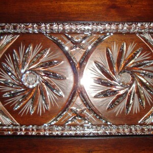 May include: A clear glass serving tray with two sections, each featuring a swirling, etched design. The tray has two handles on the sides.
