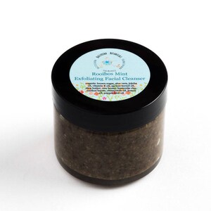 May include: A glass jar with a black lid containing a brown exfoliating facial cleanser. The label on the jar reads "Rooibos Mint Exfoliating Facial Cleanser" and lists the ingredients: organic brown sugar, aloe vera, jojoba oil, vitamin E oil, apricot kernel oil, shea butter, raw honey, bentonite clay, rooibos leaves, chamomile oil, lemon oil, peppermint oil.