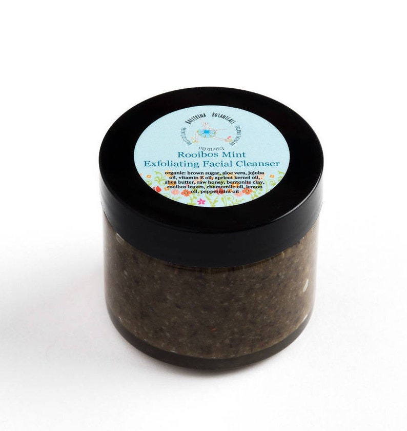 May include: A glass jar with a black lid containing a brown exfoliating facial cleanser. The label on the jar reads "Rooibos Mint Exfoliating Facial Cleanser" and lists the ingredients: organic brown sugar, aloe vera, jojoba oil, vitamin E oil, apricot kernel oil, shea butter, raw honey, bentonite clay, rooibos leaves, chamomile oil, lemon oil, peppermint oil.