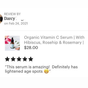 May include: A five-star review for an organic vitamin C serum with hibiscus, rosehip, and rosemary. The serum is in a clear glass bottle with a dropper. The review states "This serum is amazing! Definitely has lightened age spots."