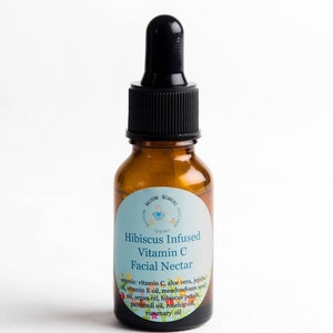 May include: A brown glass bottle with a black dropper top. The bottle has a white label with the text "Hibiscus Infused Vitamin C Facial Nectar" and a list of ingredients.