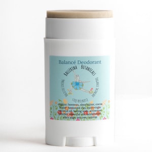 Op de afbeelding: Een witte deodorant stick met een blauw-wit etiket waarop "Balancé Deodorant Ballerina Botanicals Holistic Living Organic Skincare Stio Wellness" staat. Het etiket bevat ook een tekening van een ballerina in een blauwe tutu.