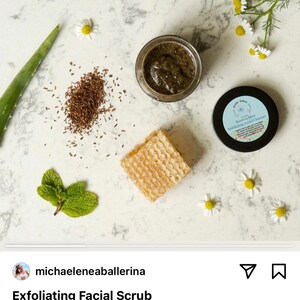 May include: A close-up of a small jar of green facial scrub with a white label that reads "Rooibos Mint Exfoliating Facial Cleanser". The jar is surrounded by small white flowers, green leaves, and a piece of honeycomb.