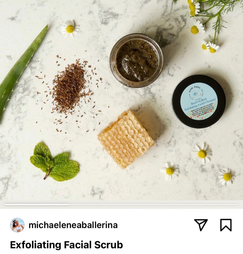 May include: A close-up of a small jar of green facial scrub with a white label that reads "Rooibos Mint Exfoliating Facial Cleanser". The jar is surrounded by small white flowers, green leaves, and a piece of honeycomb.