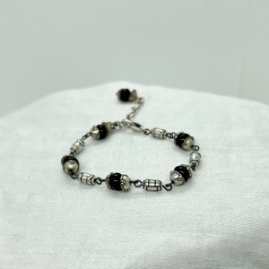 Puede incluir: Un brazalete de plata con cuentas negras y blancas. El brazalete tiene un cierre de broche.