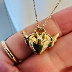 K&ouml;nnte beinhalten: Eine goldfarbene Halskette mit einem herzf&ouml;rmigen Anh&auml;nger mit Fl&uuml;geln. Der Anh&auml;nger hat ge&auml;tzte Details und eine filigrane Kette. Die Halskette ist mit "925 AU" markiert.