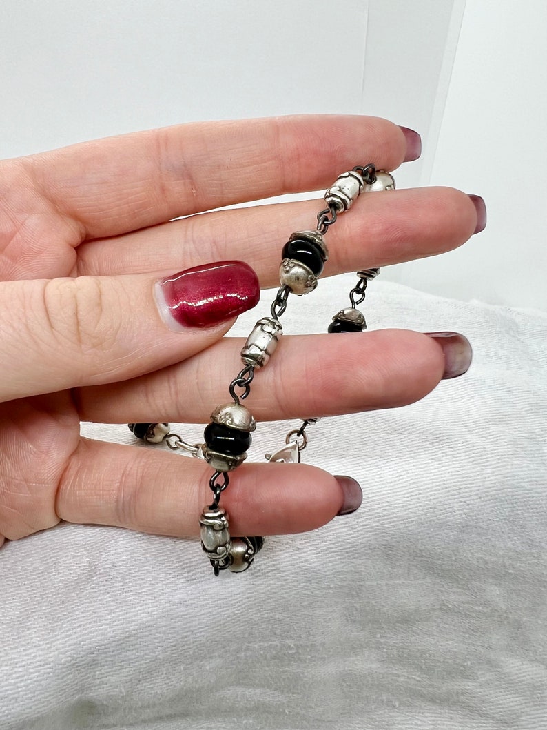 Puede incluir: Un brazalete de cadena de plata con cuentas negras. El brazalete tiene un cierre de plata y est&aacute; hecho de metal.
