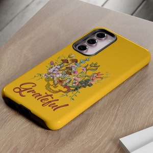 May include: A yellow phone case with a floral design and the word "Grateful" in red lettering.