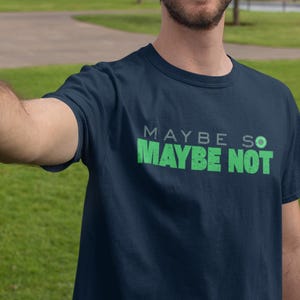 Może przedstawiać: Granatowa koszulka z zielonym napisem "MAYBE SO MAYBE NOT". Koszulka ma okrągły dekolt i jest noszona na zewnątrz w słoneczny dzień.