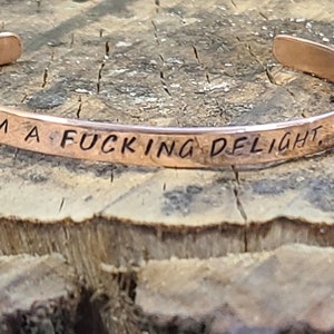 May include: A copper bracelet with the inscription "I'm a fucking delight."