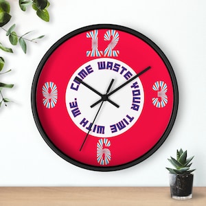 May include: A red wall clock with black hands and a white face. The clock face has the words "Waste your time with me" written in a circle around the numbers. The numbers are in a colorful, striped design.