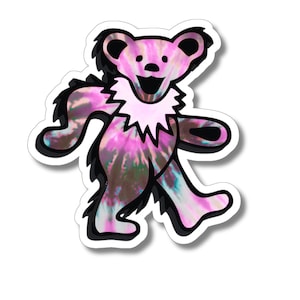May include: A pink, black, and white tie-dye bear sticker with a smiling face. The bear is walking and has a white fur collar.