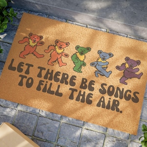 May include: A brown coir doormat with the text "Let there be songs to fill the air." and five dancing bears in different colors. The bears are in a line from left to right, with the first bear being red, the second orange, the third green, the fourth blue, and the fifth purple.