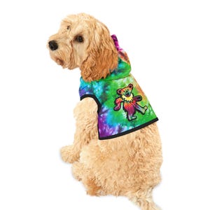 May include: A dog wearing a tie-dye hoodie with a colorful bear graphic. The hoodie features a vibrant mix of green, blue, and purple hues, with a black trim. The bear graphic is in the center of the hoodie.