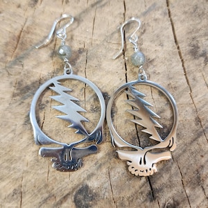 May include: Silver earrings with a lightning bolt skull design and a grey gemstone dangle.