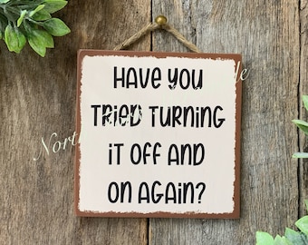 May include: A rustic wooden sign with a distressed brown background and white text. The sign reads "Have you tried turning it off and on again?"