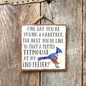 May include: Square wooden sign with a humorous quote about aging, featuring a blue and brown tufted titmouse illustration. The sign is hung by a natural rope and set against a rustic wooden background.